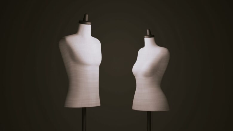 暗い背景に立つ、男性用と女性用の2体の白いトルソー【コラム】メンズとレディース、フリーランスパタンナーがパターンの違いを解説